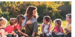 a teacher surrounded by young children outside