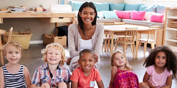 Group photo of teacher smiling with preschool students in classroom