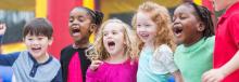 Group of children from different backgrounds singing or shouting during a game with smiles on their faces.