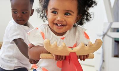 Toddler girl laughing and riding on a pony toy while toddler boy holds on