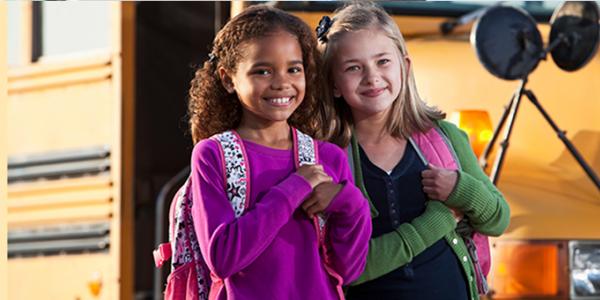 Two girls standing next to a school bus