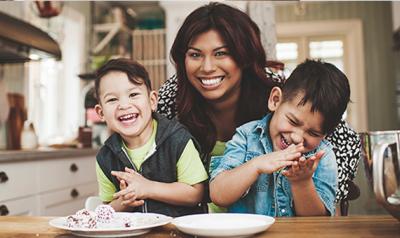 Mother hugging two sons in the kitchen that are sitting in her lap 