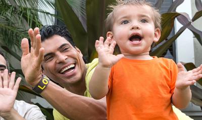 Two male parents play outdoors with their child.