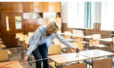 Educator measuring the distance between desk in classroom