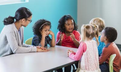 children and a teacher at a table discussing something