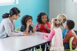 children and a teacher at a table discussing something