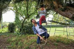 A father plays outside with their child on a rope ladder