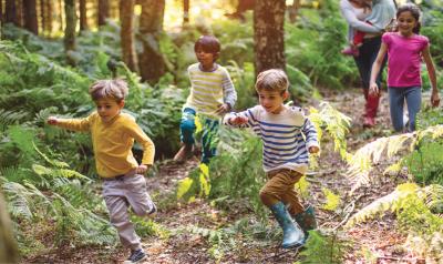 Several children run playfully through a forest.