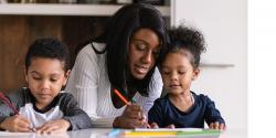 A teacher writing with children at a table.