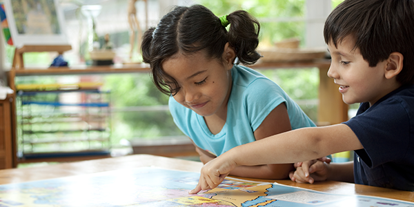 A young boy and girl pointing at a map on a desk in the classroom