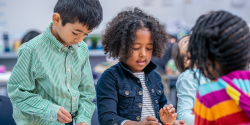 children discussing something at a table while writing