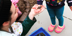 an adult handing a child a piece of mud with a worm in it