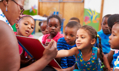 children looking at a book with a teacher